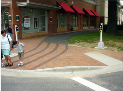 APS installed in 
            this reconstruction location in accordance with the Draft Guidlines 
            beside a level landing, within 5 feet of the crosswalk line extended 
            and less than 10 feet from the curb. The control faces and pushbuttons 
            face the intersection.