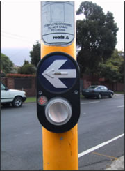 This APS has a 
              tactile arrow within a larger visible arrow. Other features include 
              a locator tone and audible and vibrotactile walk indication.